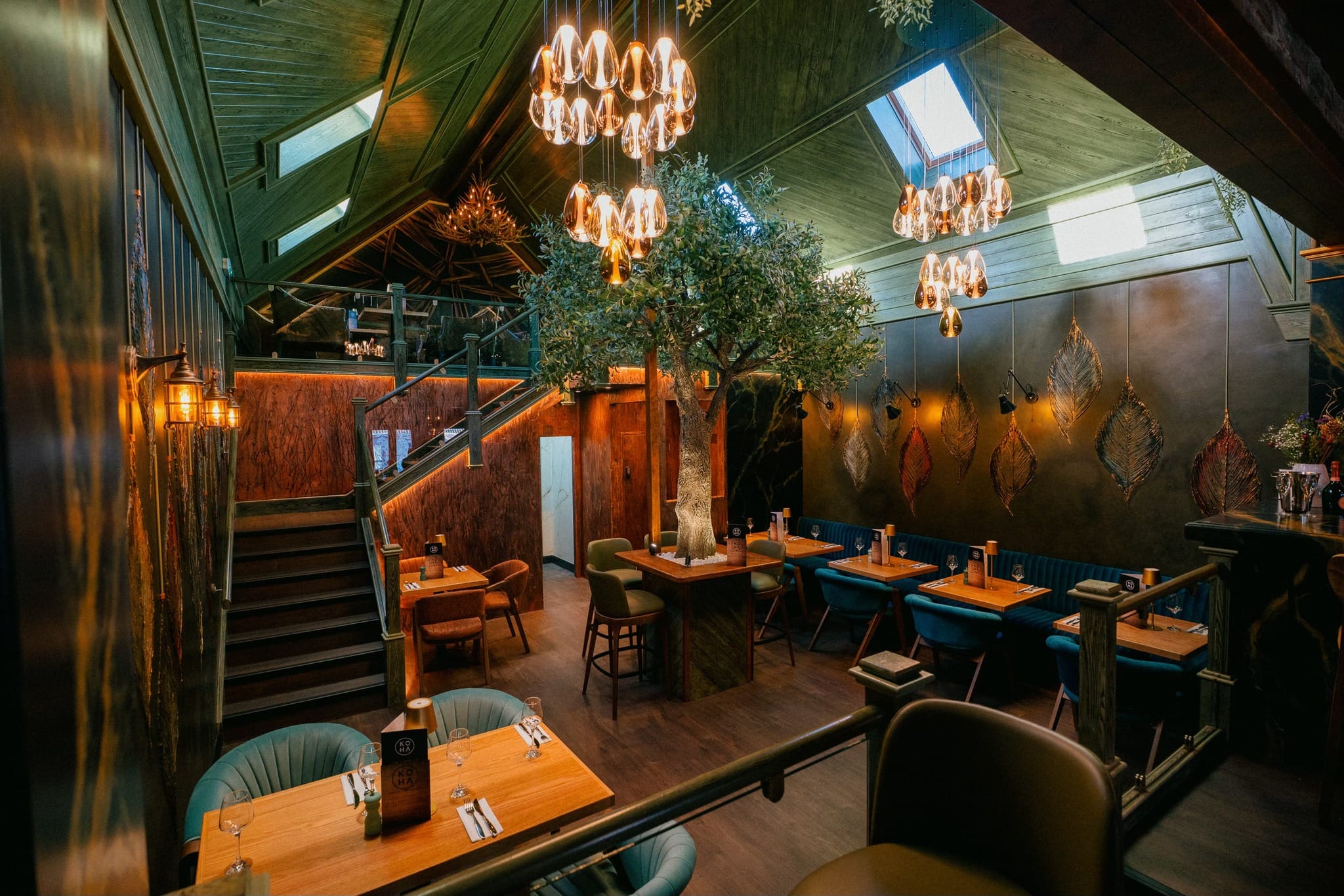 Koha restaurant interior with olive tree, elegant chandeliers, and teal booth seating
